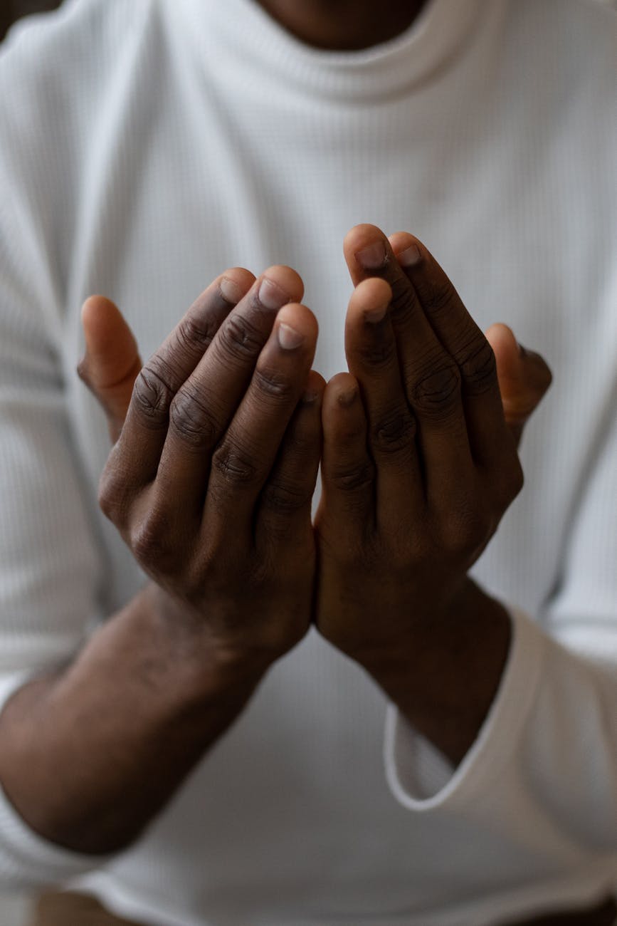 prayer, torso of a shadowed figure in a white top with upraised hands